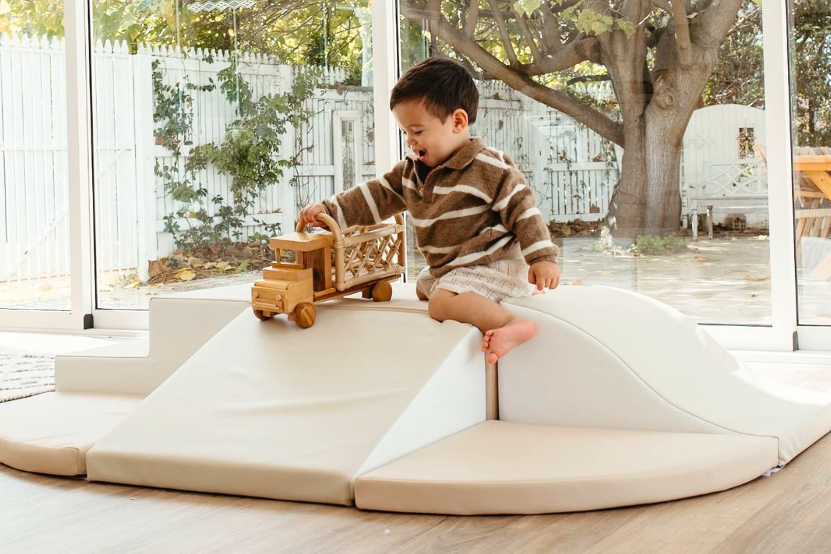 Set of large colorful foam modular climbing blocks arranged into stairs and tunnel configuration for indoor toddler active play in a Montessori-inspired playroom