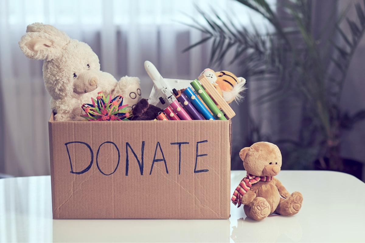A cardboard box labeled 'DONATE' filled with stuffed animals and colorful pens, representing items a Montessori mom chooses not to keep.