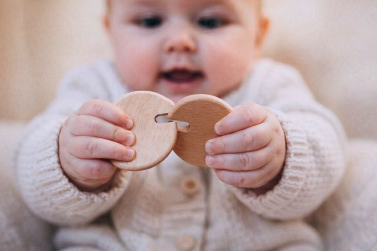 baby holding and exploring interlocking wooden rings, grasping and mouthing the toy during playtime