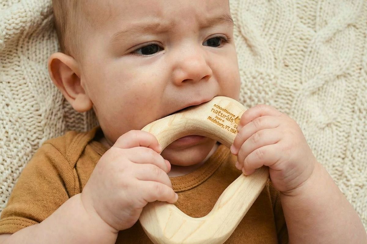 6-month-old baby chewing on a smooth maple wood teether during playtime