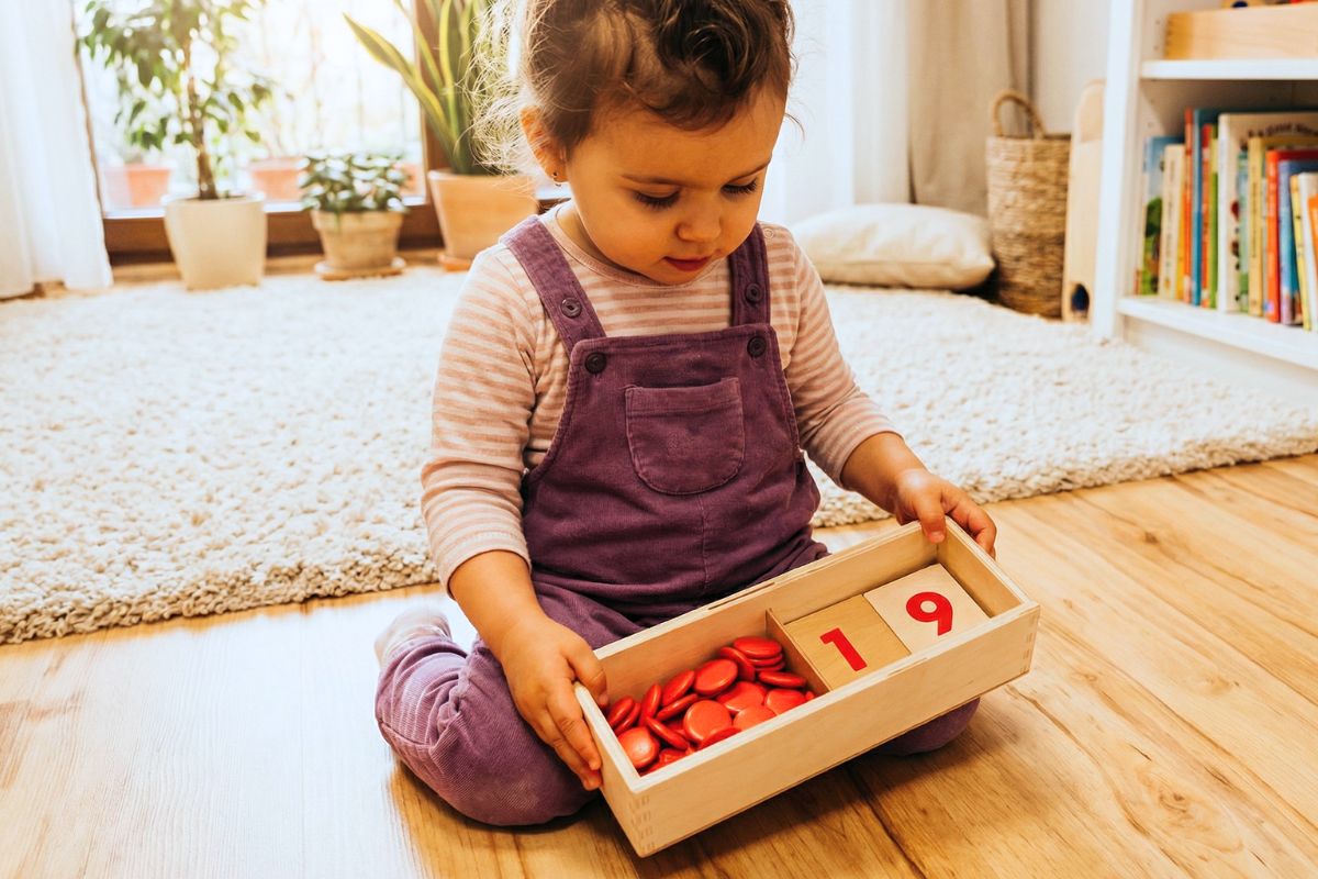 Wooden Montessori number cards 1 to 10 displayed in order alongside a box of red circular counters on a work mat