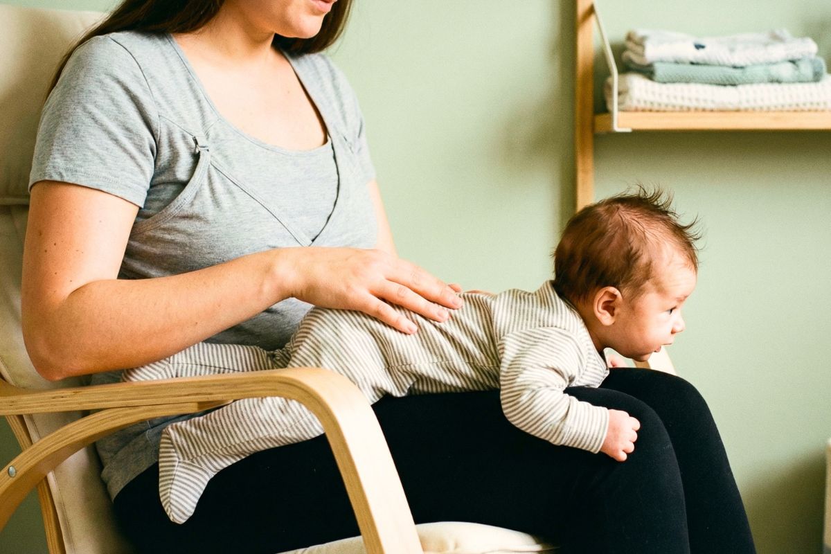 mother sitting upright her 5-week-old baby lying tummy-down across both her thighs