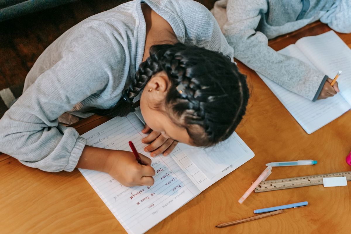 Girl with braids writing in a workbook at a classroom table