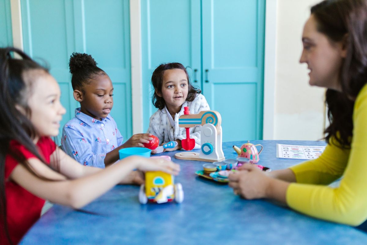 Teacher sitting at a table with three young girls playing together