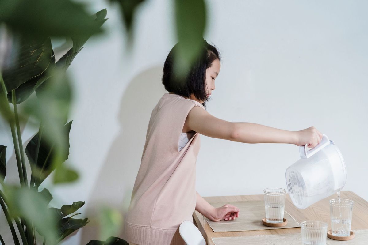 Young girl pouring water from a small pitcher into a glass at a low table