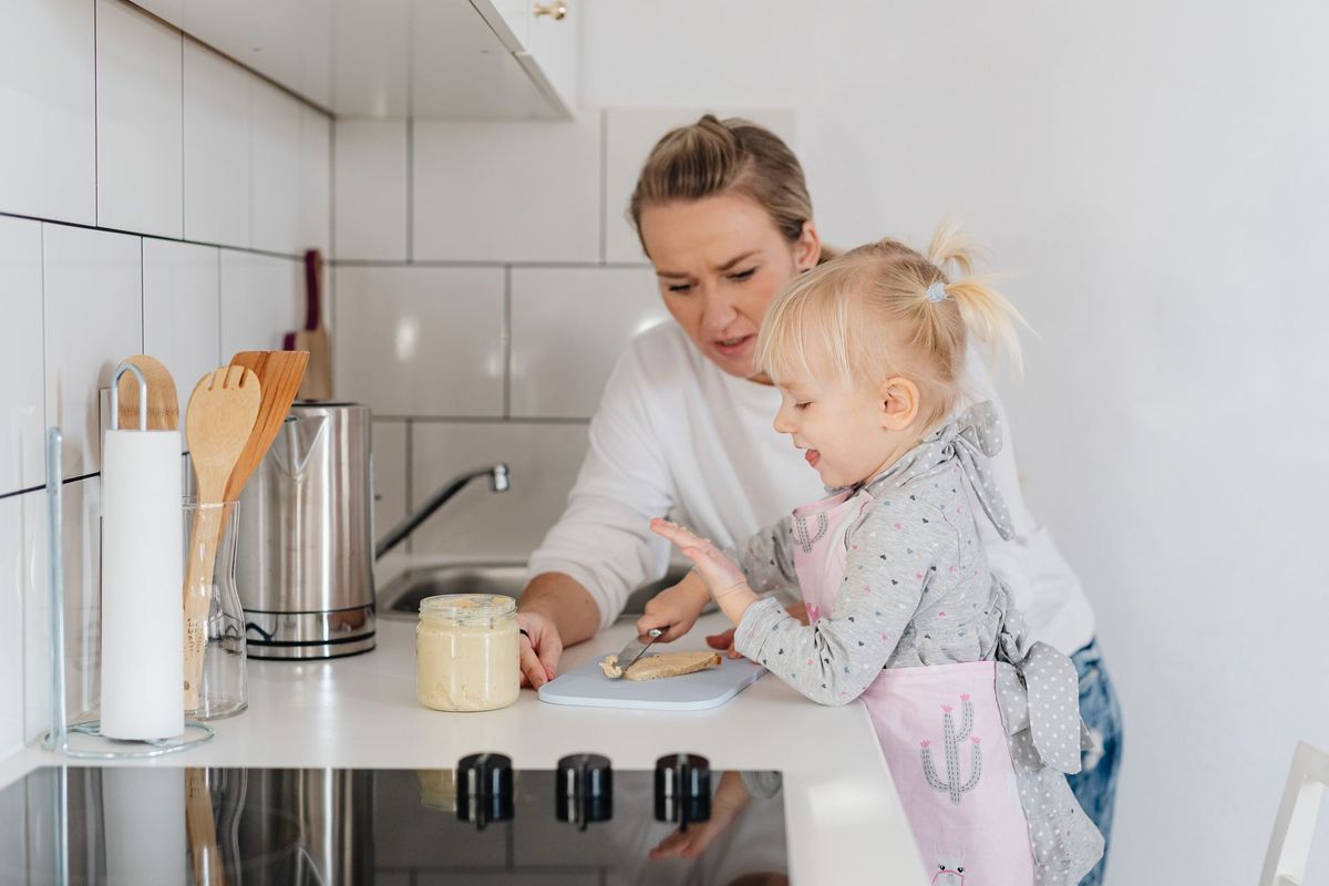 Toddler in an apron helping a parent prepare food at the kitchen counter