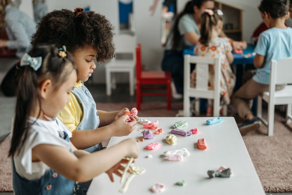 Preschoolers shaping playdough at a low table in a bright classroom
