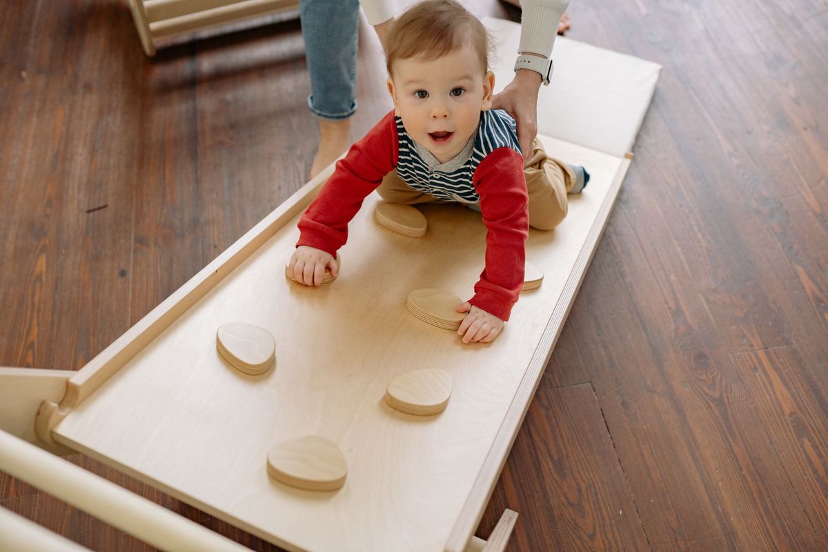 Toddler crawling on a wooden climbing board on the floor