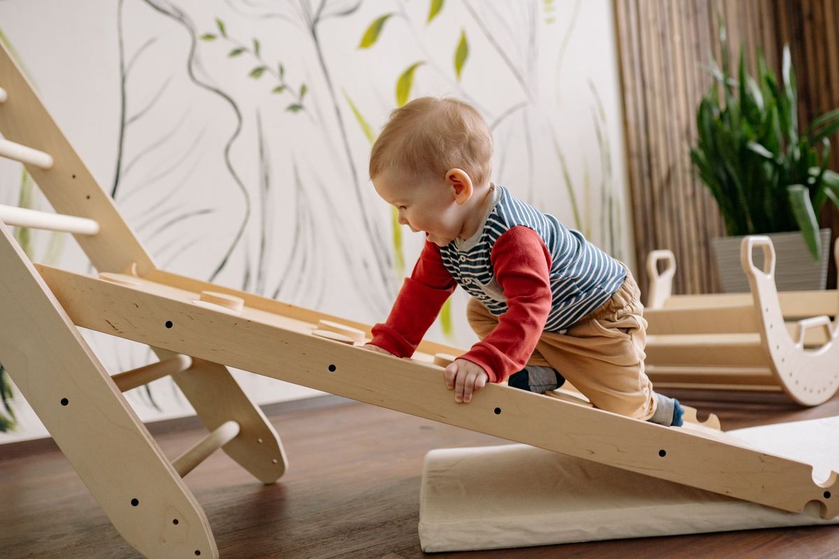 Toddler crawling up a wooden climbing ramp indoors