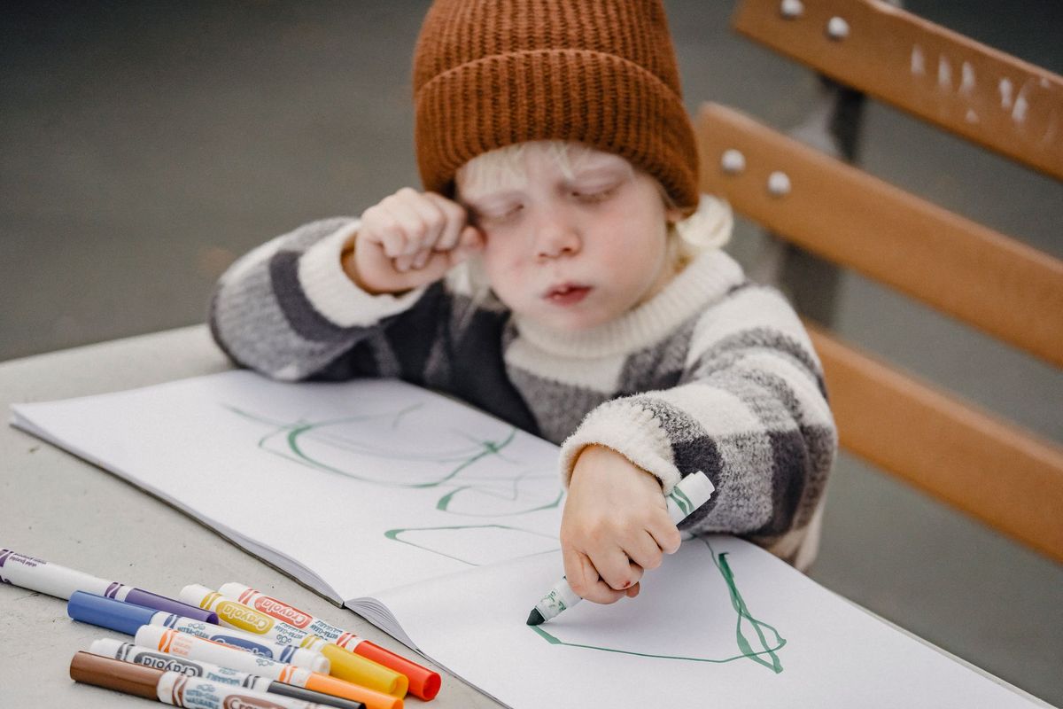 Young child in a knit hat drawing with markers on paper