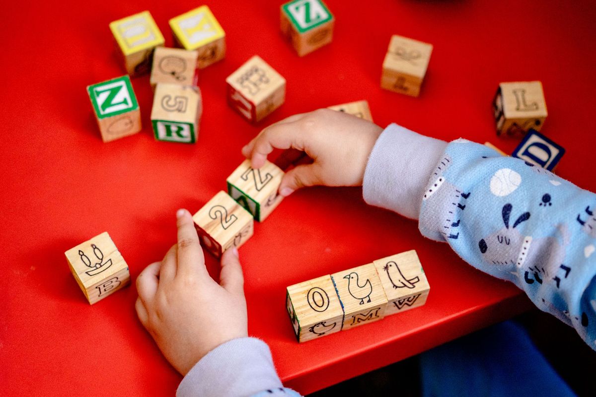 Child arranging wooden alphabet blocks on a red table